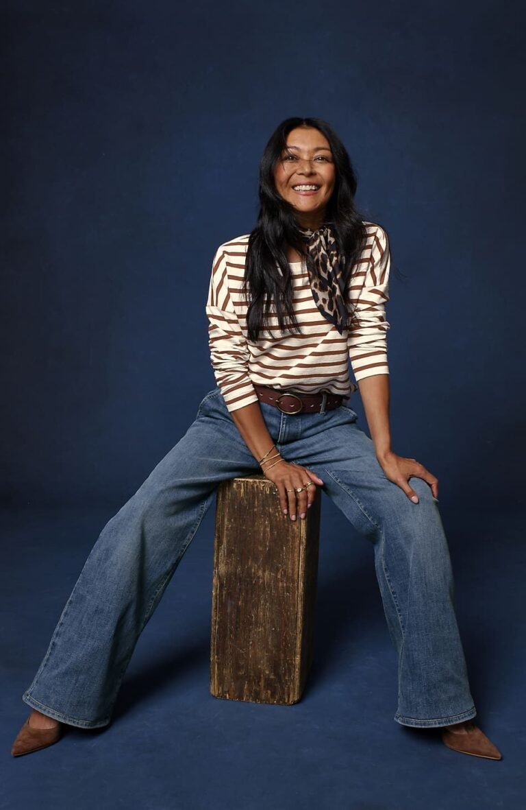 Woman over 50 wearing medium wash wide leg jeans with a fitted striped tee tucked in, a balanced denim outfit with pointed toe flats.