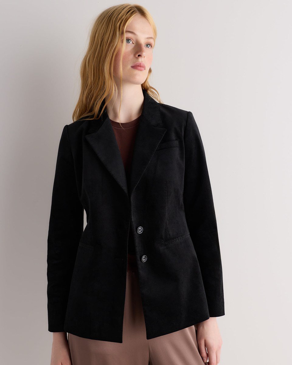 Black velvet blazer with notched lapels, the first of these velvet outfits for women over 50, worn over a dark knit top.