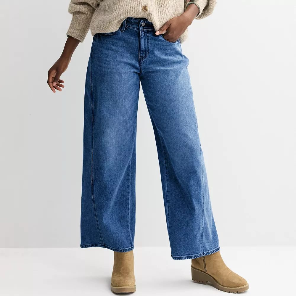 Woman over 50 wearing seamed wide leg jeans with a half tucked henley and clean sneakers, a weekend outfit.