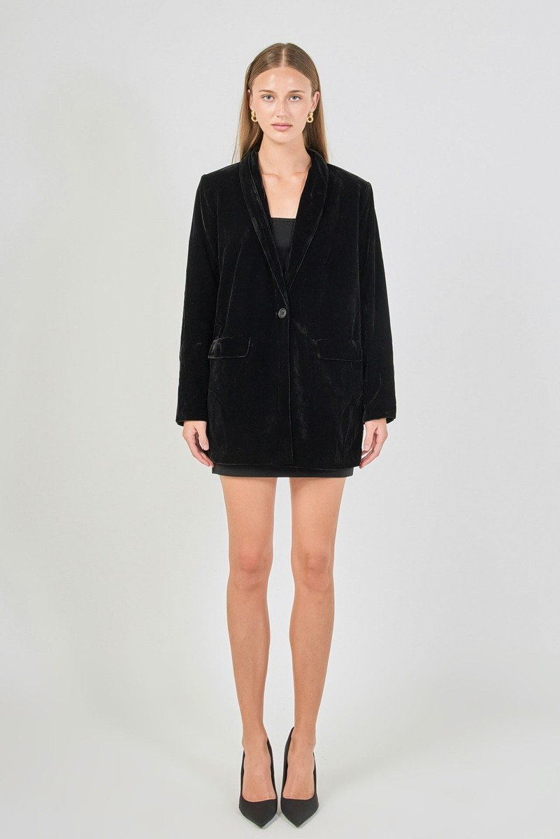 Black velvet blazer with a shawl collar and one front button, worn over a black dress.