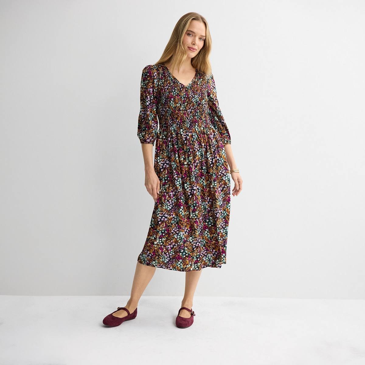 Dark floral smocked midi dress with three-quarter sleeves and a V neck, worn with burgundy flats.