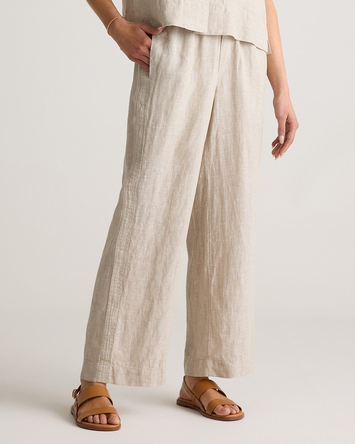 Woman over 50 wearing linen wide leg pants with a fitted tank top and flat sandals, a warm fall day outfit.