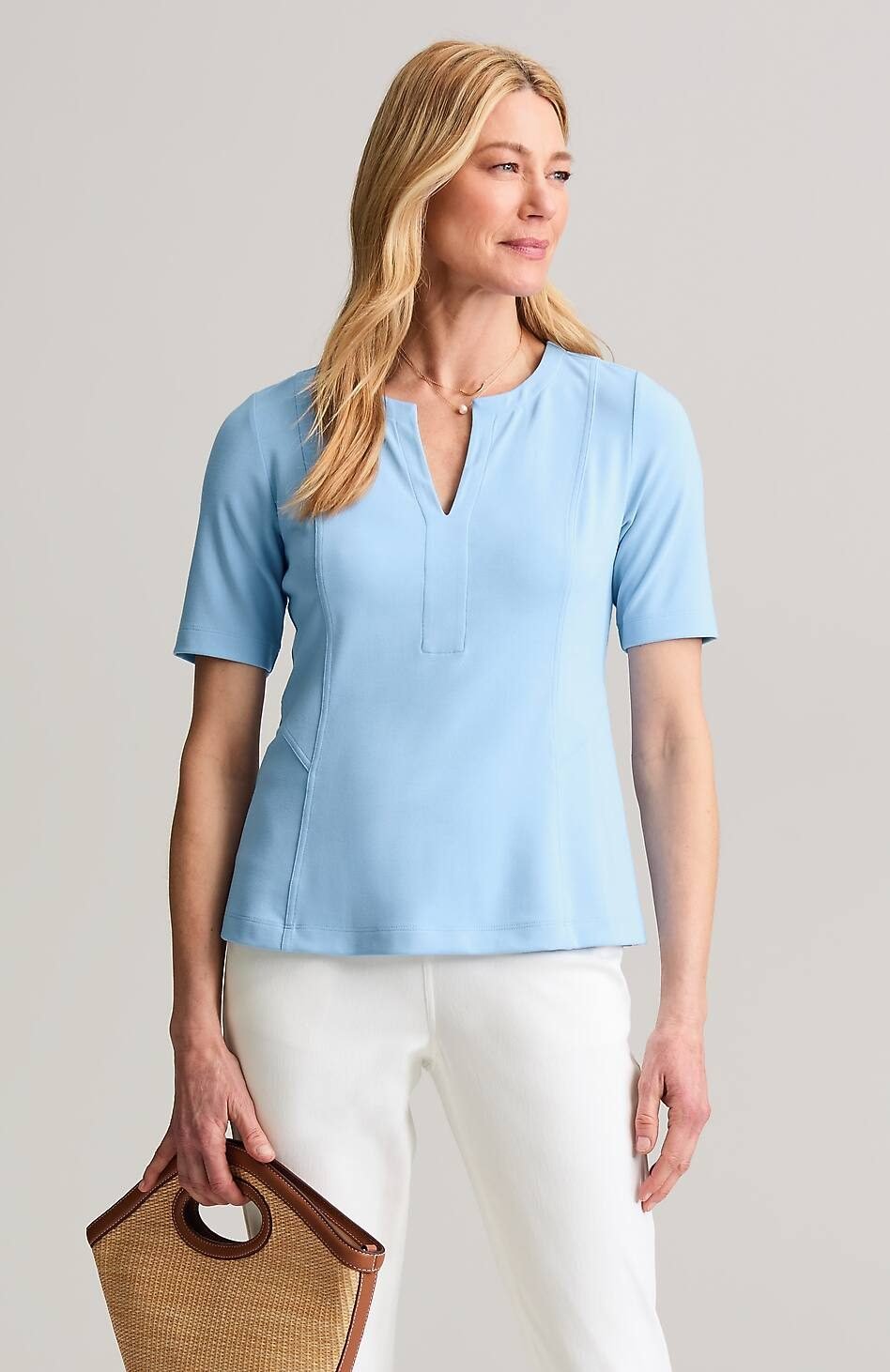 Woman over 50 wearing a light blue elbow sleeve knit top with a split neckline and white jeans.