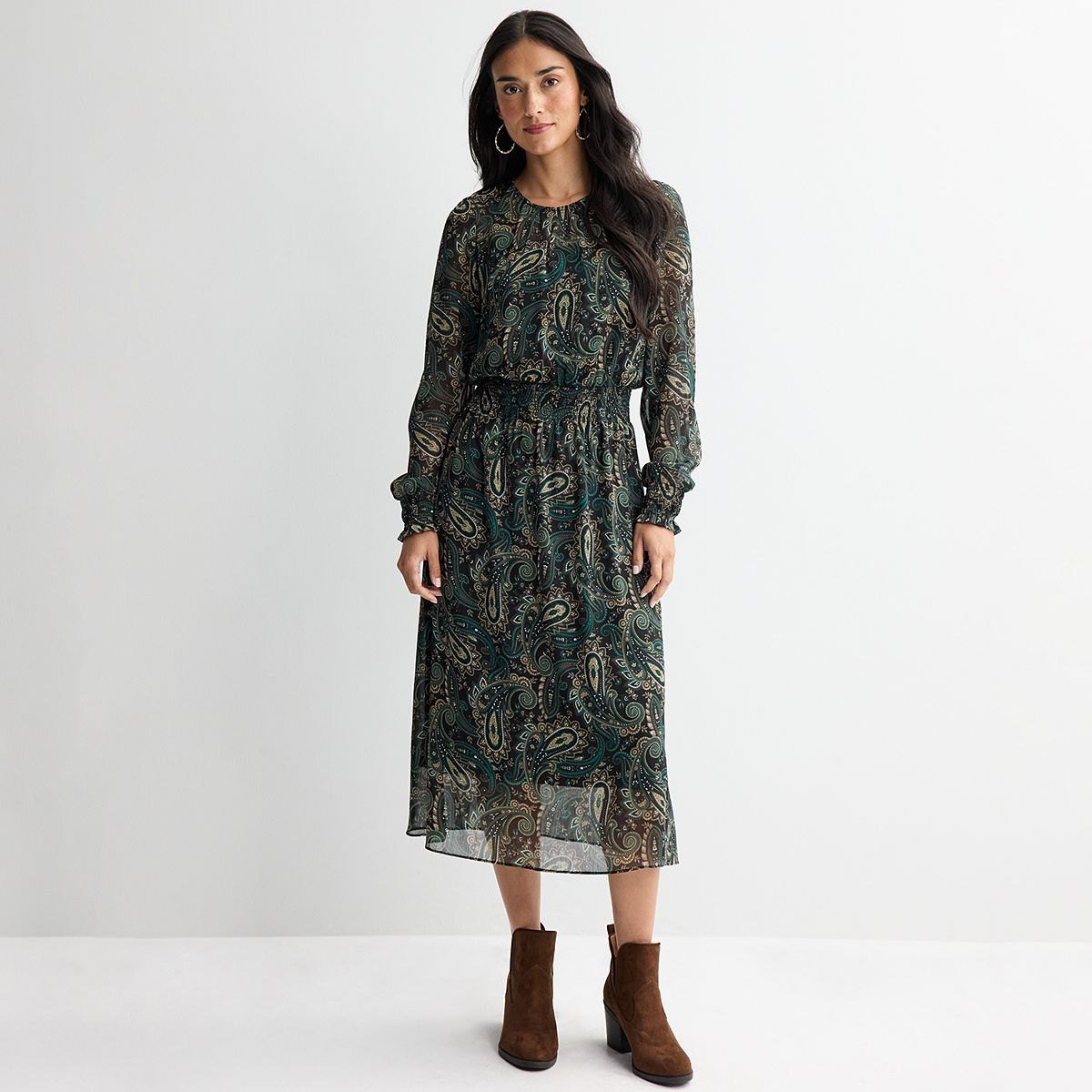 Deep green and gold paisley midi dress with long sleeves and a smocked waist, worn with brown ankle boots.