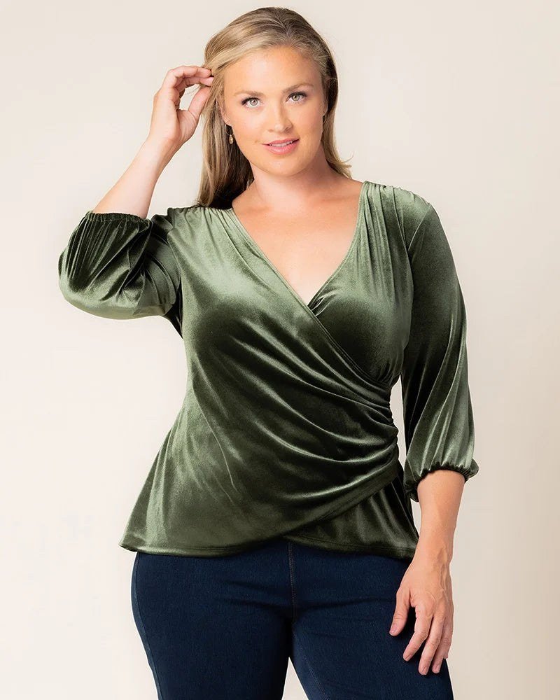 Olive green velvet faux wrap top with three quarter sleeves, worn with dark jeans by a plus size model.