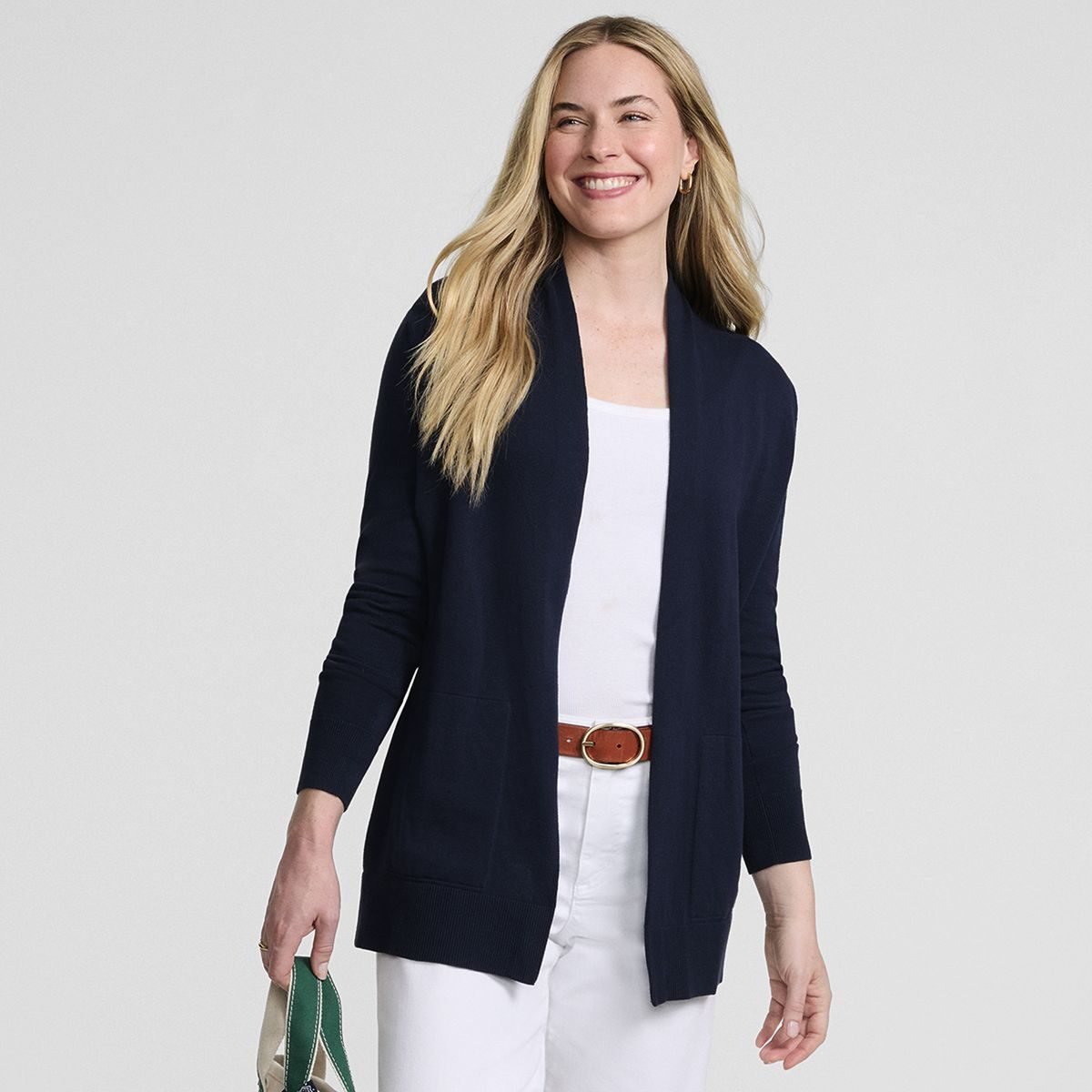Woman over 50 wearing a long navy open cardigan over a dark knit top and white jeans.