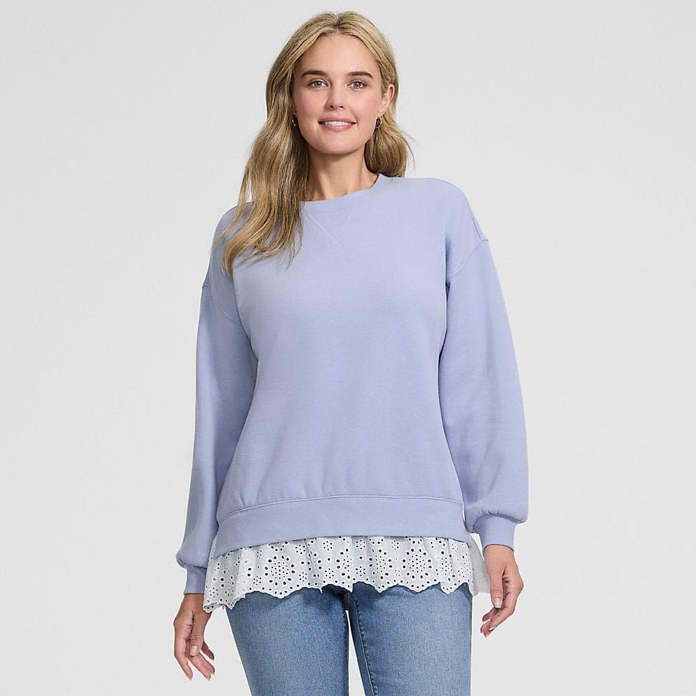 Woman over 50 in a light blue tunic sweatshirt with a lace hem worn over dark straight leg jeans, a casual Thanksgiving outfit for hosting at home.
