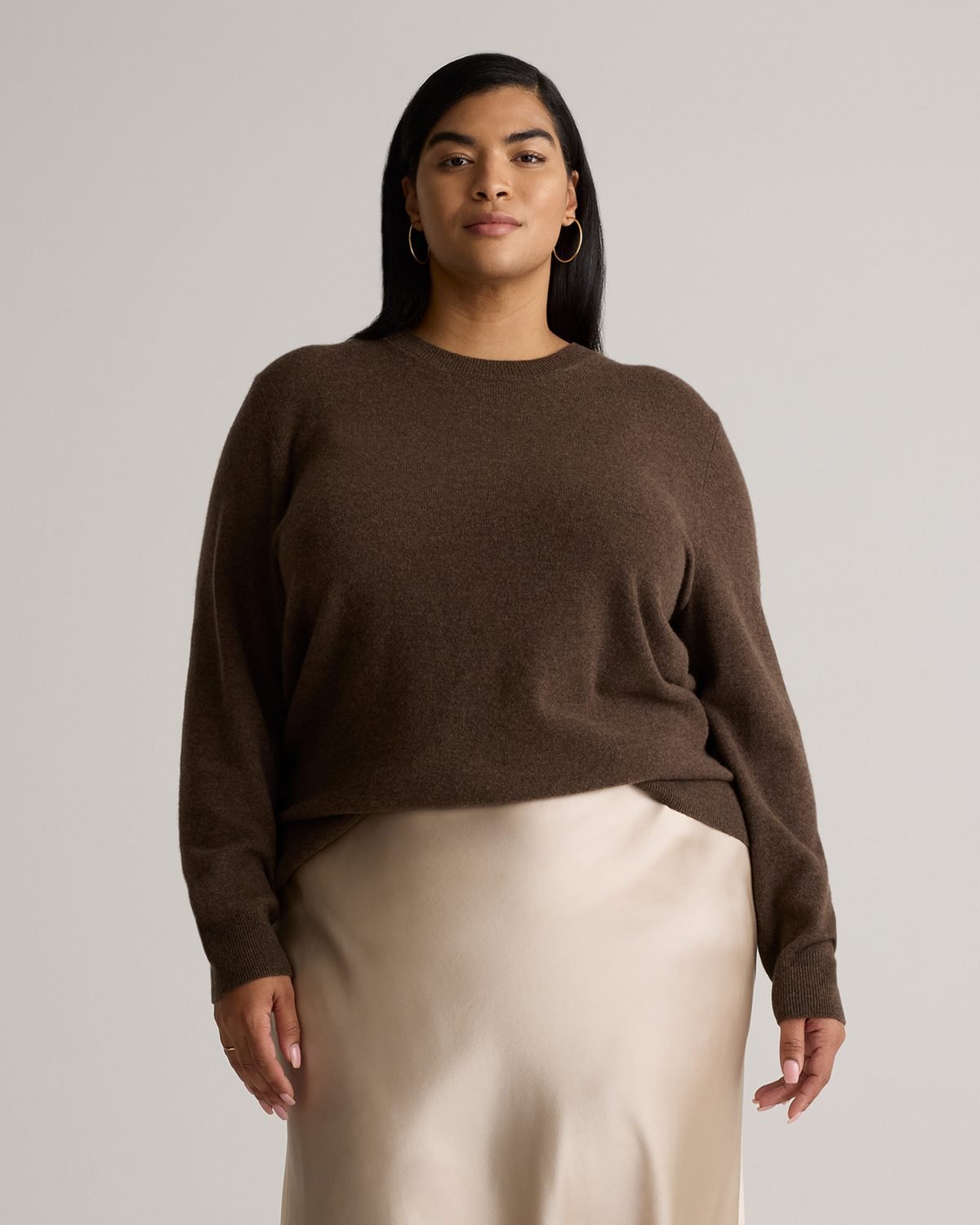 Woman over 50 wearing white high rise jeans with a chocolate brown cashmere crewneck and bit loafers.